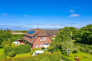 A large brick house with multiple rooms, surrounded by lush greenery and a clear blue sky.