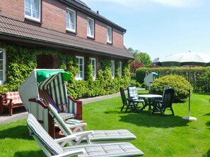 A brick house with a garden. There are lounge chairs and a table with umbrellas.