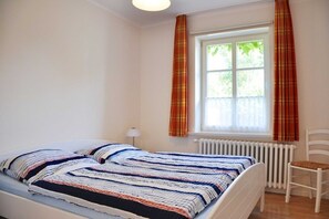A bedroom with a bed, a chair, a window with curtains, and a radiator.