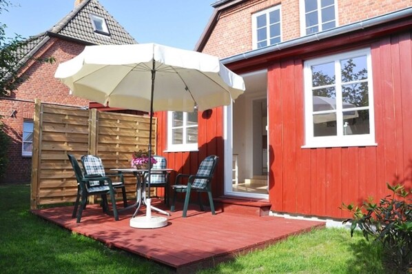 A patio with a table and chairs, a white umbrella, and a wooden fence.