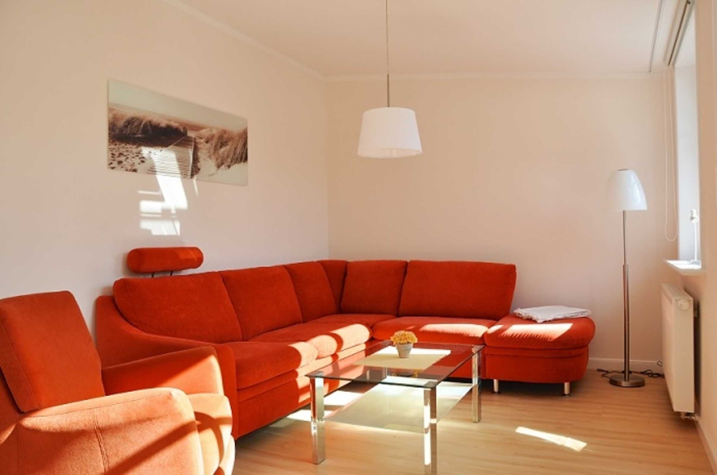 Ein modernes Wohnzimmer mit einem großen, orangefarbenen Ecksofa, einem Glastisch und einer weißen Pendelleuchte.