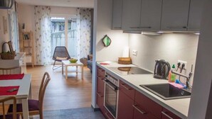 Une cuisine moderne avec des meubles rouges, un plan de travail noir et un évier. On aperçoit, au fond, un coin repas avec une table et des chaises.