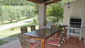 Un patio exterior con mesa y sillas de madera, un pilar de ladrillo y una parrilla empotrada.