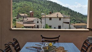 A balcony with a table set for dining, overlooking a village with traditional buildings and a forested hillside. - Casa Raissa C: A characteristic and welcoming apartment that is part of a villa immersed in a splendid landscape, in a lovely little hamlet, with Free WI-FI. (Montaione)