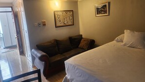 Una habitación con una cama, un sofá, una mesa y una silla. Hay dos cuadros en la pared.