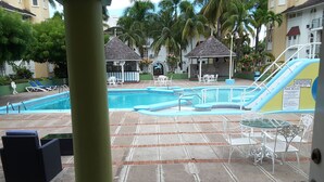 Un área de piscina con sillones de descanso, un pequeño pabellón y un tobogán.