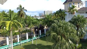 Un patio con palmeras, una cerca verde y un edificio de techo oscuro.