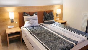 Camera d'albergo con un letto, abat-jour, comodino, una testiera in legno e un quadro raffigurante un paesaggio sopra il letto.