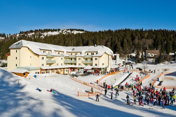 A ski resort with a large building, ski slopes, and a crowd of people.