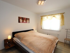 A bedroom with a bed, bedside lamps, a radiator, a window with curtains, and a painting on the wall.
