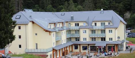 Ein mehrstöckiges Hotel mit Balkonen, einer überdachten Außenlounge und Blick auf ein bewaldetes Gebiet.