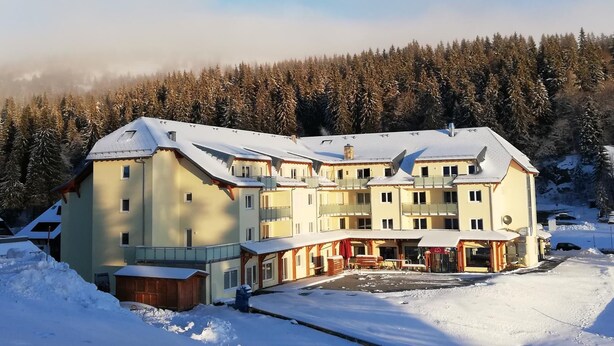 A large, multi-story hotel with a snow-covered roof and a forested backdrop.