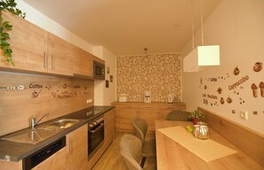 A kitchen with wooden cabinets, a built-in stove, a sink, and a dining area with a table and chairs. - GRA-312 - Modern vacation apartment with whirlpool (HT) - Residence Grafenmatt 3.2 (Feldberg (Schwarzwald))
