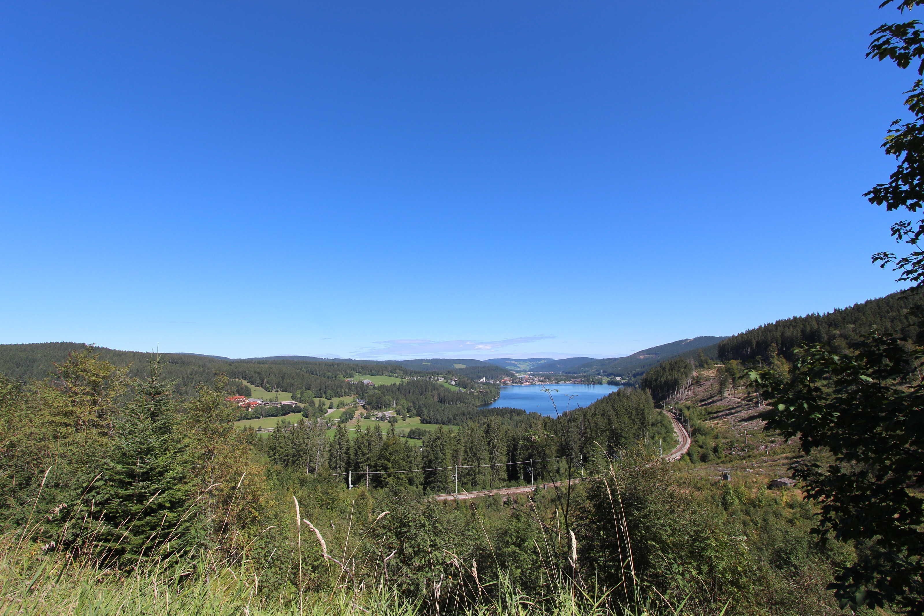 A mountainous landscape with a lake, forested areas, and a winding road.