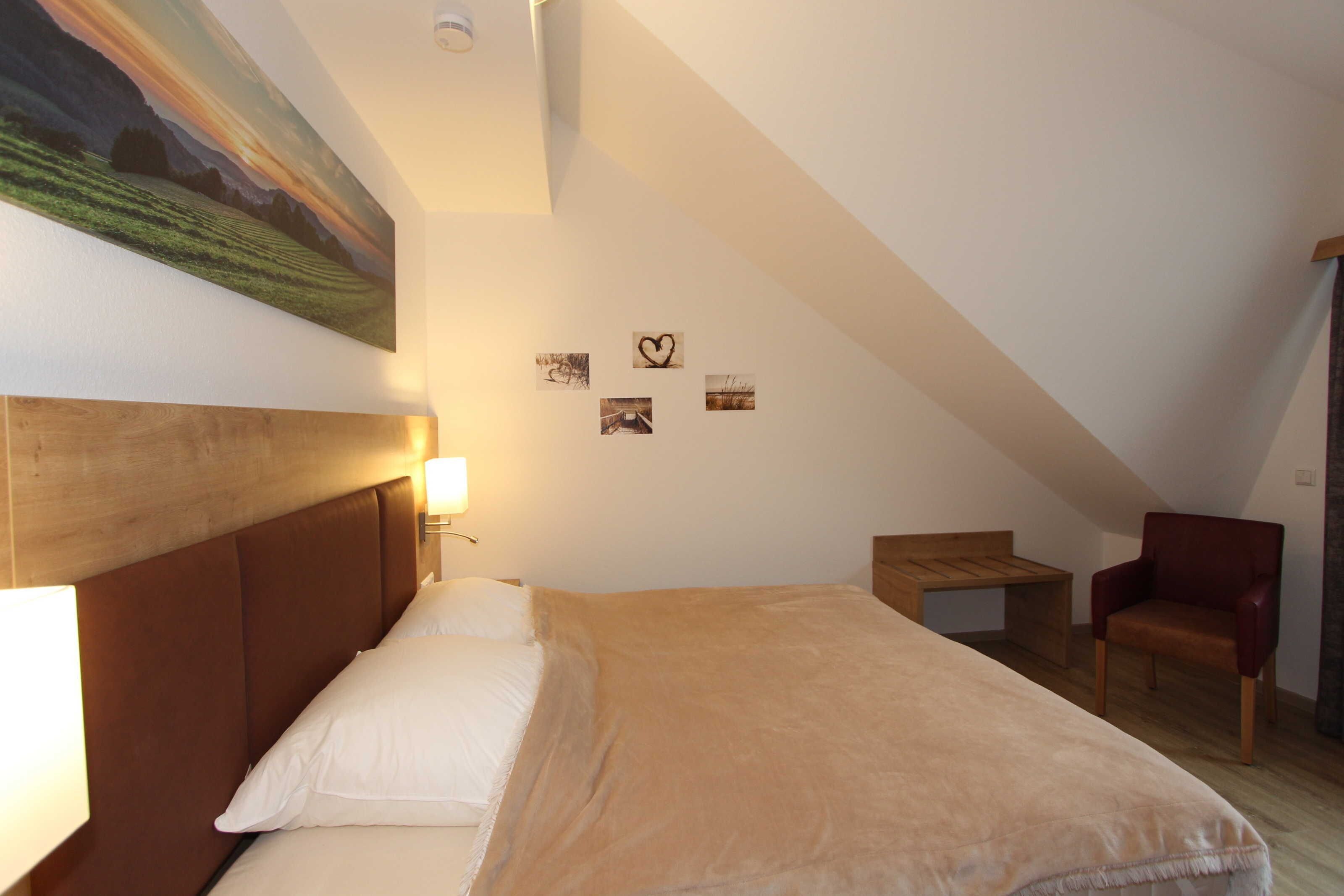 Un dormitorio con una cama, una silla, una mesita y un cuadro en la pared.