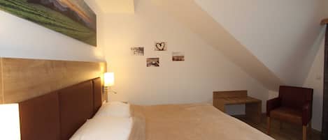 Un dormitorio con una cama, una silla, una mesita y un cuadro en la pared.