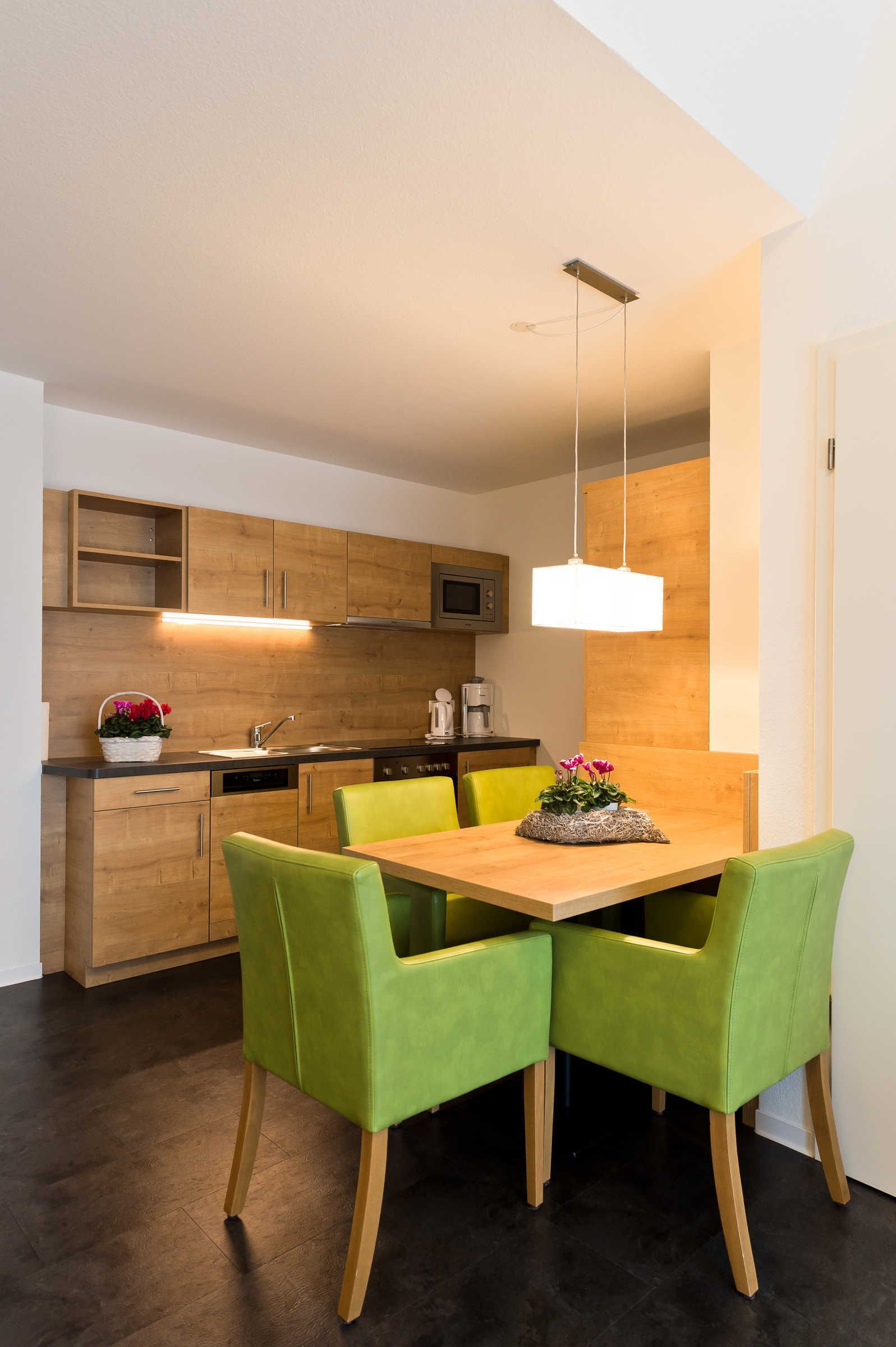 A modern kitchen with wooden cabinets, a dining table with green chairs, and a pendant light.