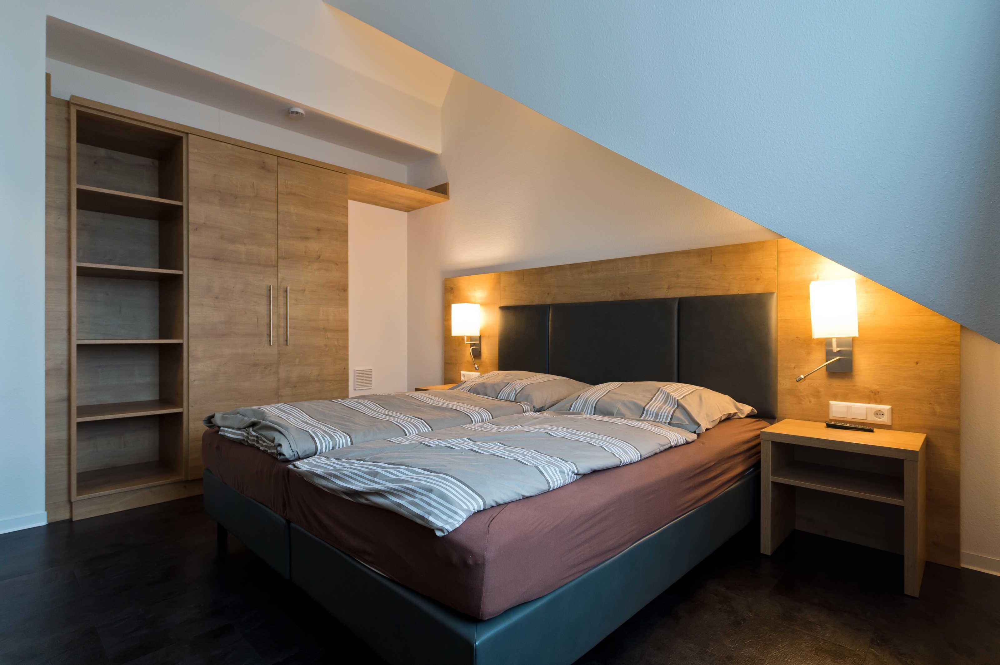 A bedroom with a bed, wooden wardrobe, nightstands, and a sloped ceiling.