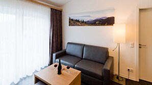 En moderne stue med en sofa, et sofabord med vinglas og en flaske, en lampe og et landskabsmaleri på væggen.