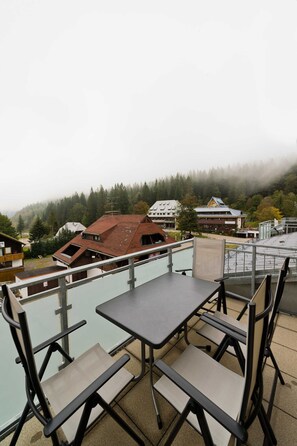 Una terraza con mobiliario exterior, vistas a edificios y una ladera cubierta de bosque.