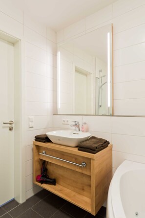 Un baño moderno con lavamanos blanco, tocador de madera y un espejo grande.