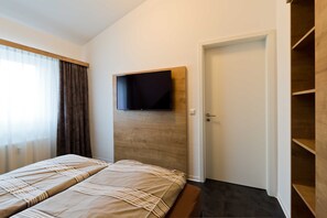 A hotel room with a bed, a mounted TV, a door, and a wooden shelf unit. - GRA-303 - Vacation apartment with hot tub and sauna (excl. tax) - Grafenmatt 3.1 Residence (Feldberg (Schwarzwald))