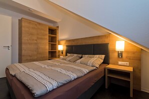 Un dormitorio con cama, armario de madera, lámparas de noche y mesita de noche.