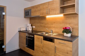 Una cocina moderna con armarios de madera, microondas integrado, cafetera, pileta y una planta en maceta.