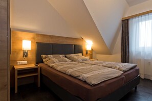 Un dormitorio con cama, lámparas de noche, mesita de noche y ventana con cortinas.