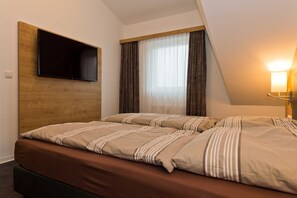 Ein Hotelzimmer mit einem Bett, einem Wandfernseher, einem Fenster mit Vorhängen und einer Nachttischlampe.