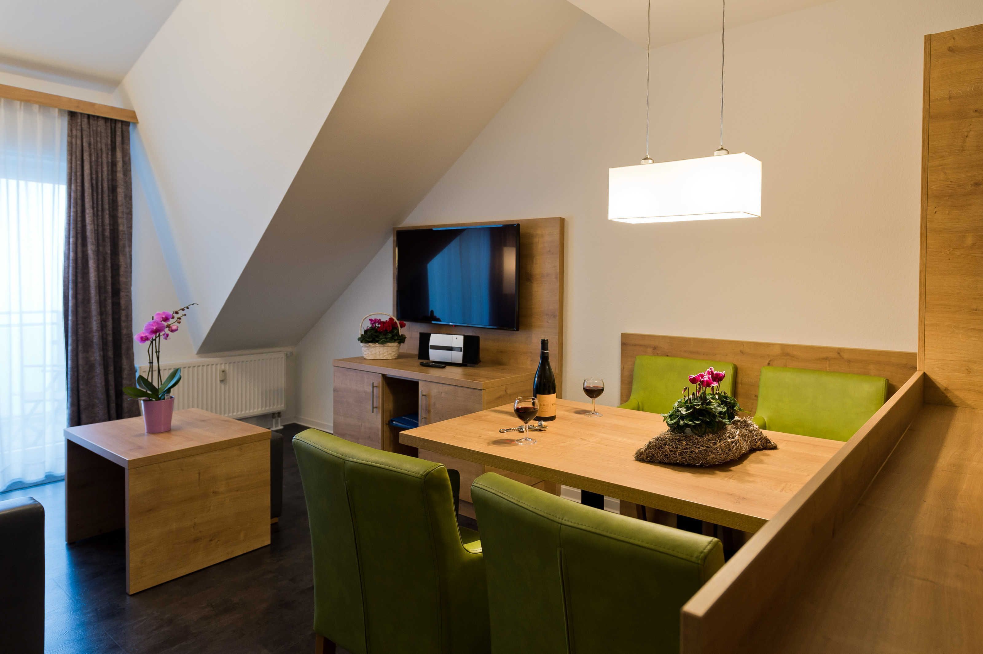 Una habitación moderna con una mesa de comedor, sillas verdes, un televisor y un mueble de madera.
