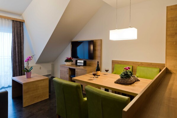 Een moderne kamer met een eettafel, groene stoelen, een televisie en een houten kast.