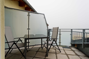 Un balcon avec une table et des chaises, une paroi en verre et une vue sur la mer.