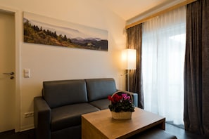 A room with a sofa, a table with a flower basket, a lamp, and a painting on the wall.