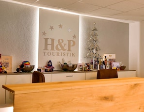 Un espace d’accueil avec une enseigne indiquant « H&P TOURISTIK », un sapin de Noël décoratif et divers objets exposés sur le comptoir.