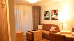Un salon comprenant un canapé, une table basse et un coin repas avec des chaises. Deux tableaux encadrés ornent le mur.