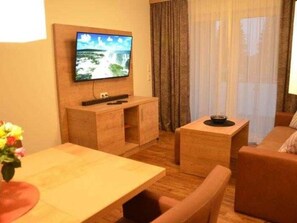 Een hotelkamer met een houten tv-standaard, een flatscreen televisie, een houten tafeltje, een bank en een raam met gordijnen.