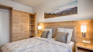 A bedroom with a bed, wooden wardrobe, bedside lamps, and a landscape painting on the wall. - GRA-006 Gipfelglück vacation apartment with whirlpool & terrace - Grafenmatt Residence (Feldberg (Schwarzwald))