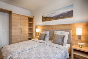 Une chambre à coucher avec un lit, une armoire en bois, des lampes de chevet et un tableau représentant un paysage accroché au mur.