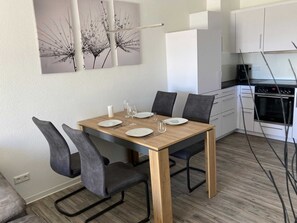 Un comedor con una mesa de madera, cuatro sillas y una cocina al fondo.