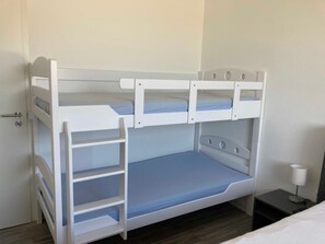 Un lit superposé avec une échelle, une table de chevet avec une lampe et une porte.