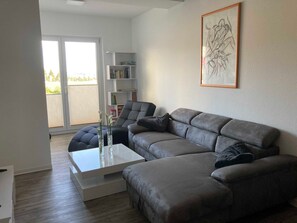 Un salon moderne avec un canapé d’angle gris, une table basse blanche et une bibliothèque.