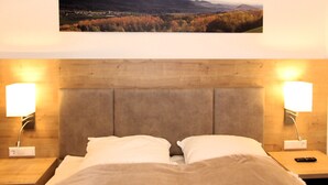 Un lit avec deux oreillers, une tête de lit en bois, des lampes de chevet et un tableau représentant un paysage au-dessus du lit.