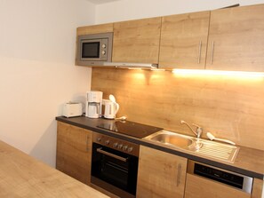 A compact kitchen with wooden cabinets, a microwave, a coffee maker, a toaster, a sink, and an oven. - GRA-210 - Vacation apartment with south-east-facing balcony and whirlpool - Grafenmatt Residence (Feldberg (Schwarzwald))
