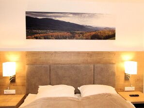A bed with two pillows, a wooden headboard, bedside lamps, and a landscape picture above the bed.
