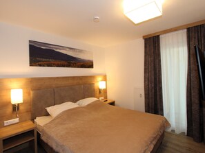 Ein Hotelzimmer mit Bett, Nachttischlampen, einem Nachttisch, einem Bild an der Wand und einem Fenster mit Vorhängen.