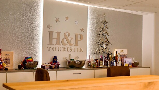 Un espace d’accueil avec une enseigne indiquant « H&P TOURISTIK », un sapin de Noël décoratif et divers objets exposés sur le comptoir.