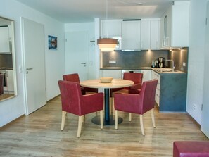 Une cuisine compacte avec des meubles blancs, une table ronde entourée de quatre chaises et un petit îlot central doté d’un évier.