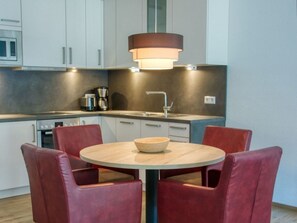 Una cocina moderna con armarios blancos, una mesa redonda con cuatro sillas rojas, una cafetera y una lámpara colgante.