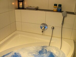 Una vasca da bagno con una doccetta, una candela e due flaconi su uno scaffale.